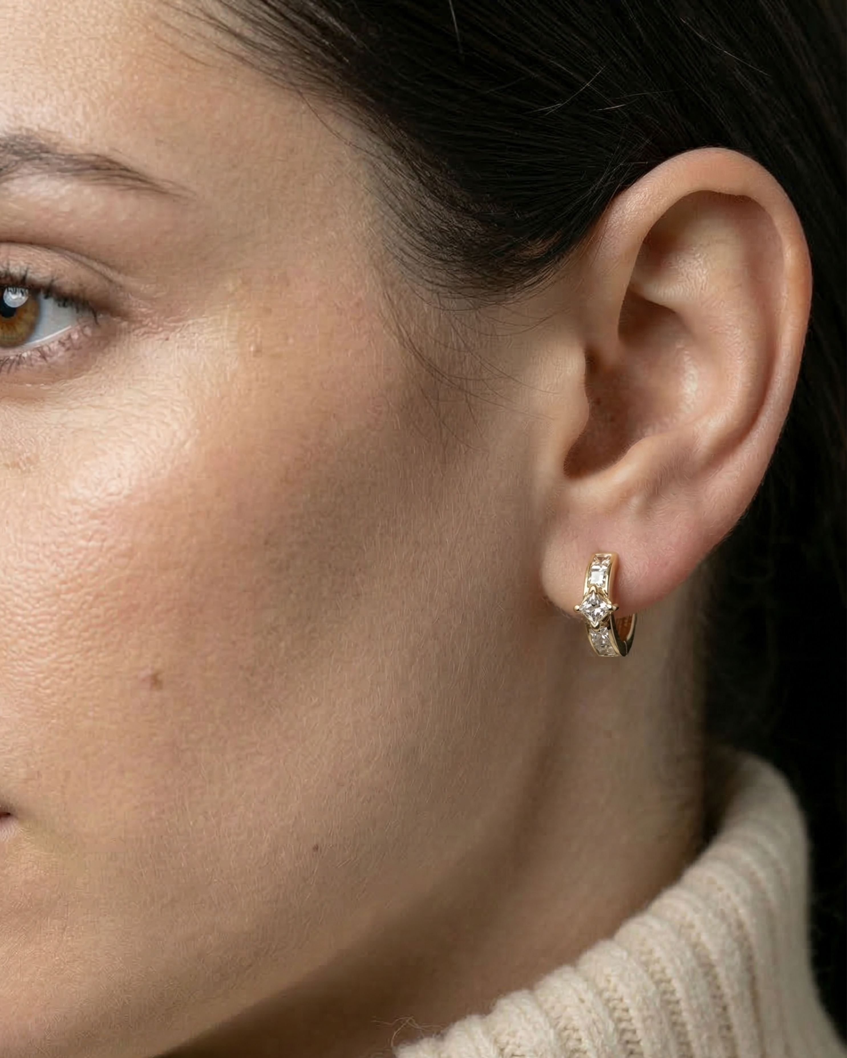 Close-up of a model's ear wearing the 14k gold Modernist Princess Cut Diamond Hoop with channel-set stones.