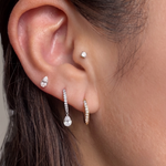 Close-up of a model's ear wearing the Floating Pear Diamond Stud, styled with other diamond hoop and stud earrings.