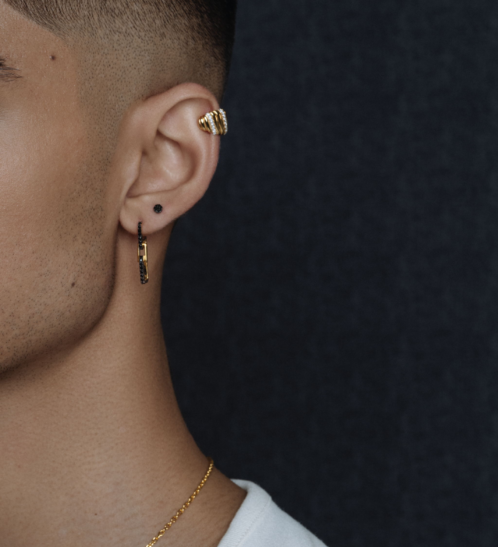 Close-up on a model's ear wearing the gold Palm Diamond Ear Cuff on the helix, styled with other earrings.